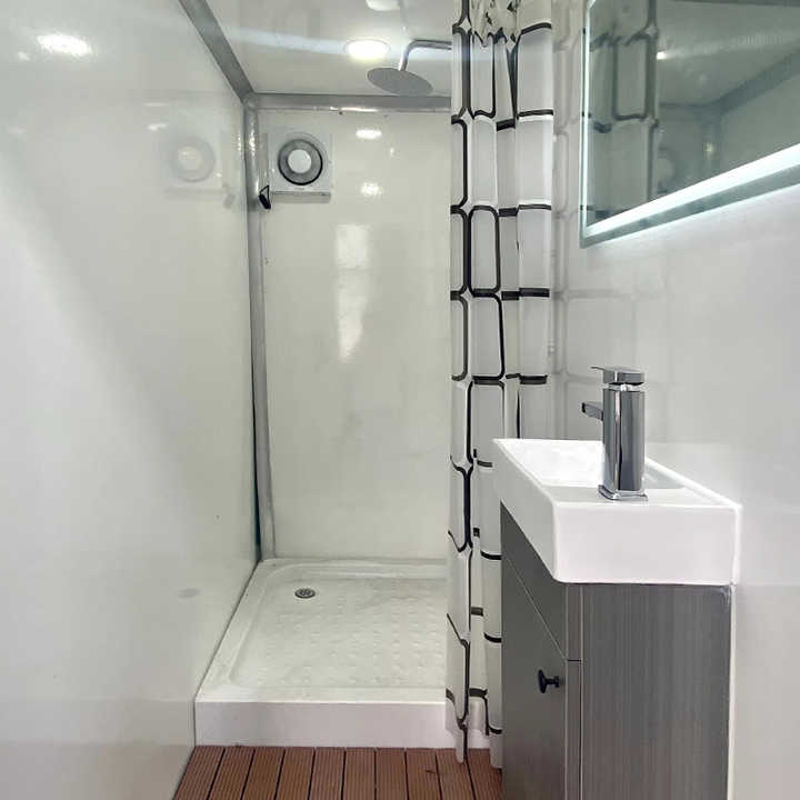Shower compartment with a curtain, wall vent, mirror, and compact handwashing sink
