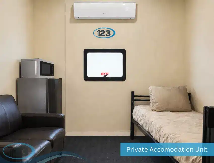 Private accommodation unit featuring a single bed, leather sofa, mini refrigerator, microwave, wall-mounted air conditioner, and window inside a climate-controlled modular sleeper container.